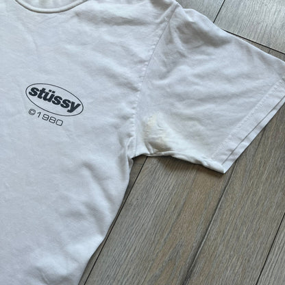 Stussy Soul 1980 White Tee is a white short-sleeve T-shirt released as part of a spring drop, made from soft cotton with a relaxed fit and ribbed collar. The front features a small Stussy logo print on the chest, while the back includes black Stussy text, a large multicolor central graphic, and “Copyright 1980” text at the bottom.