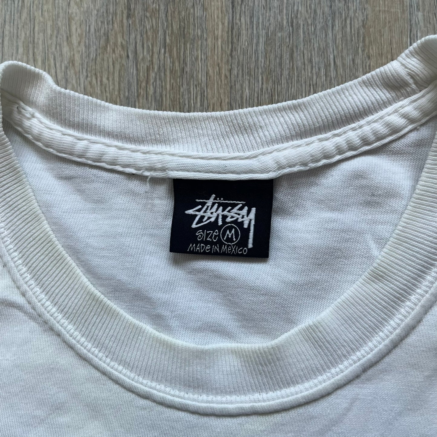 Stussy Soul 1980 White Tee is a white short-sleeve T-shirt released as part of a spring drop, made from soft cotton with a relaxed fit and ribbed collar. The front features a small Stussy logo print on the chest, while the back includes black Stussy text, a large multicolor central graphic, and “Copyright 1980” text at the bottom.