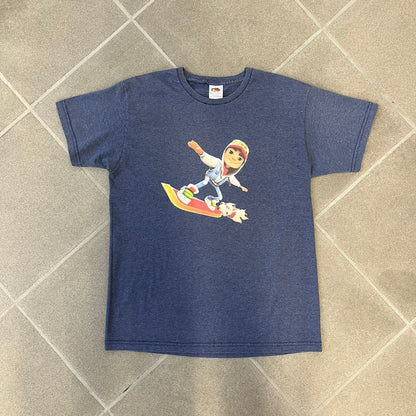 Subway Surfers 2010s Jake Tee is a grey T-shirt made on a Fruit of the Loom blank. The front features Jake, the main character from Subway Surfers, riding his skateboard, with the pursuing guard dog biting the end of the board. The design is printed in full color on the front.
