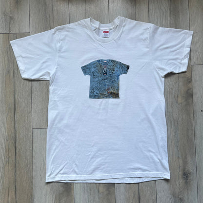 Supreme 30th Anniversary SS24 First Tee is a white T-shirt released on April 25, 2024, as part of the SS24 season. The front features a small OG Taxi Driver Supreme shirt graphic in blue with graffiti-style detailing. Below the back collar, a small gray tag displays the Supreme 30th Anniversary logo.