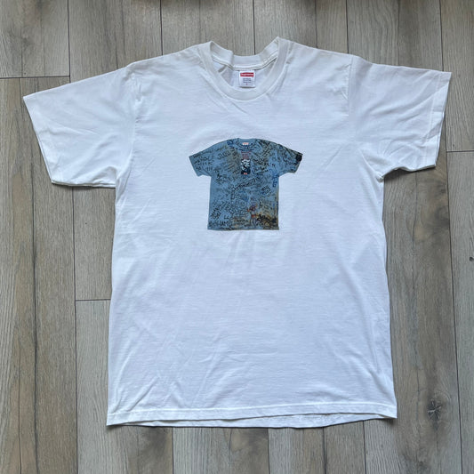 Supreme 30th Anniversary SS24 First Tee is a white T-shirt released on April 25, 2024, as part of the SS24 season. The front features a small OG Taxi Driver Supreme shirt graphic in blue with graffiti-style detailing. Below the back collar, a small gray tag displays the Supreme 30th Anniversary logo.