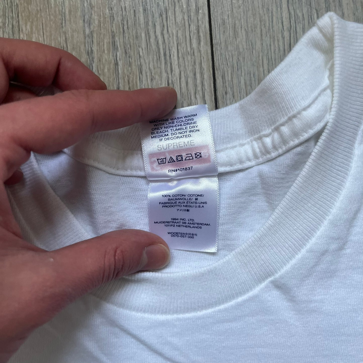 Supreme 30th Anniversary SS24 First Tee is a white T-shirt released on April 25, 2024, as part of the SS24 season. The front features a small OG Taxi Driver Supreme shirt graphic in blue with graffiti-style detailing. Below the back collar, a small gray tag displays the Supreme 30th Anniversary logo.