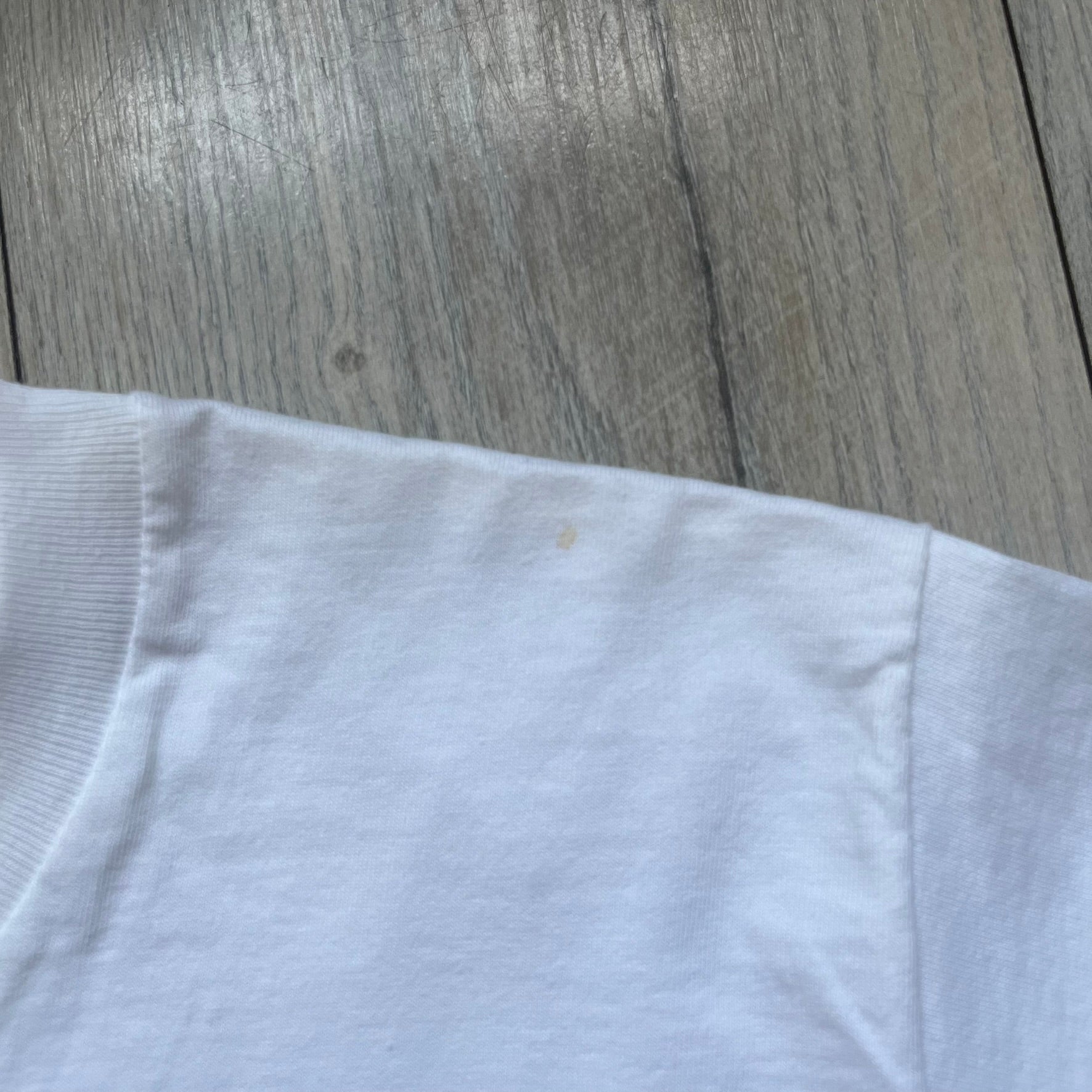 Supreme 30th Anniversary SS24 First Tee is a white T-shirt released on April 25, 2024, as part of the SS24 season. The front features a small OG Taxi Driver Supreme shirt graphic in blue with graffiti-style detailing. Below the back collar, a small gray tag displays the Supreme 30th Anniversary logo.