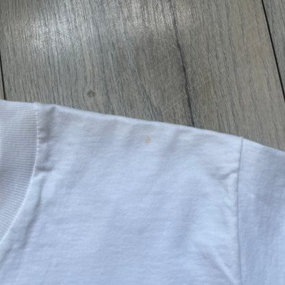 Supreme 30th Anniversary SS24 First Tee is a white T-shirt released on April 25, 2024, as part of the SS24 season. The front features a small OG Taxi Driver Supreme shirt graphic in blue with graffiti-style detailing. Below the back collar, a small gray tag displays the Supreme 30th Anniversary logo.