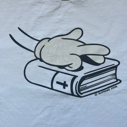 Supreme SS06 Oath White Tee is a white short-sleeve T-shirt from the Spring/Summer 2006 collection. The front features a black outline graphic of a Mickey Mouse-style hand placed on a cartoon Bible with a visible cross, with small “Supreme 2006” copyright text on the side. Super rare piece.