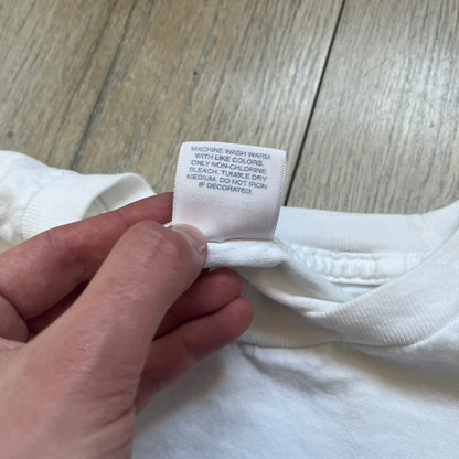 Supreme SS06 Oath White Tee is a white short-sleeve T-shirt from the Spring/Summer 2006 collection. The front features a black outline graphic of a Mickey Mouse-style hand placed on a cartoon Bible with a visible cross, with small “Supreme 2006” copyright text on the side. Super rare piece.