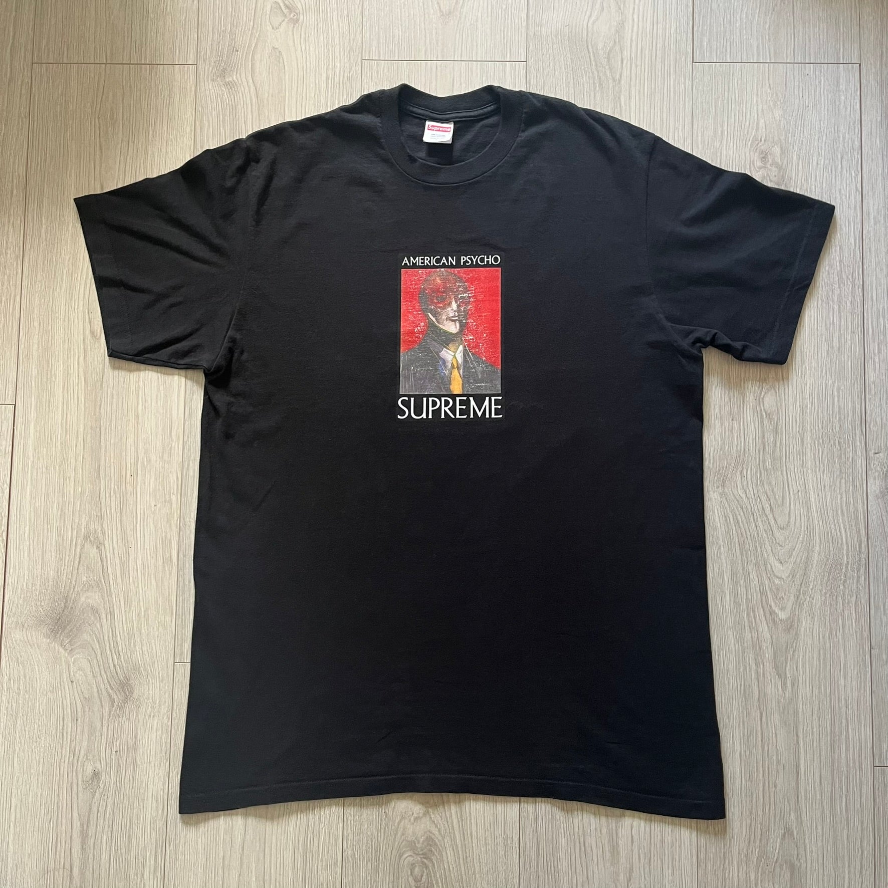 Supreme FW23 “American Psycho” tee in black, released October 2023. Features a large front print of Marshall Arisman’s iconic cover art for Bret Easton Ellis’s novel American Psycho, with big SUPREME text beneath. A standout graphic piece that merges literature, art, and streetwear.