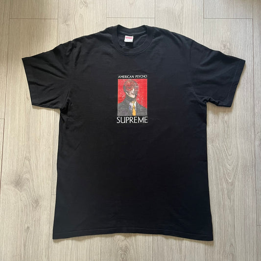Supreme FW23 “American Psycho” tee in black, released October 2023. Features a large front print of Marshall Arisman’s iconic cover art for Bret Easton Ellis’s novel American Psycho, with big SUPREME text beneath. A standout graphic piece that merges literature, art, and streetwear.