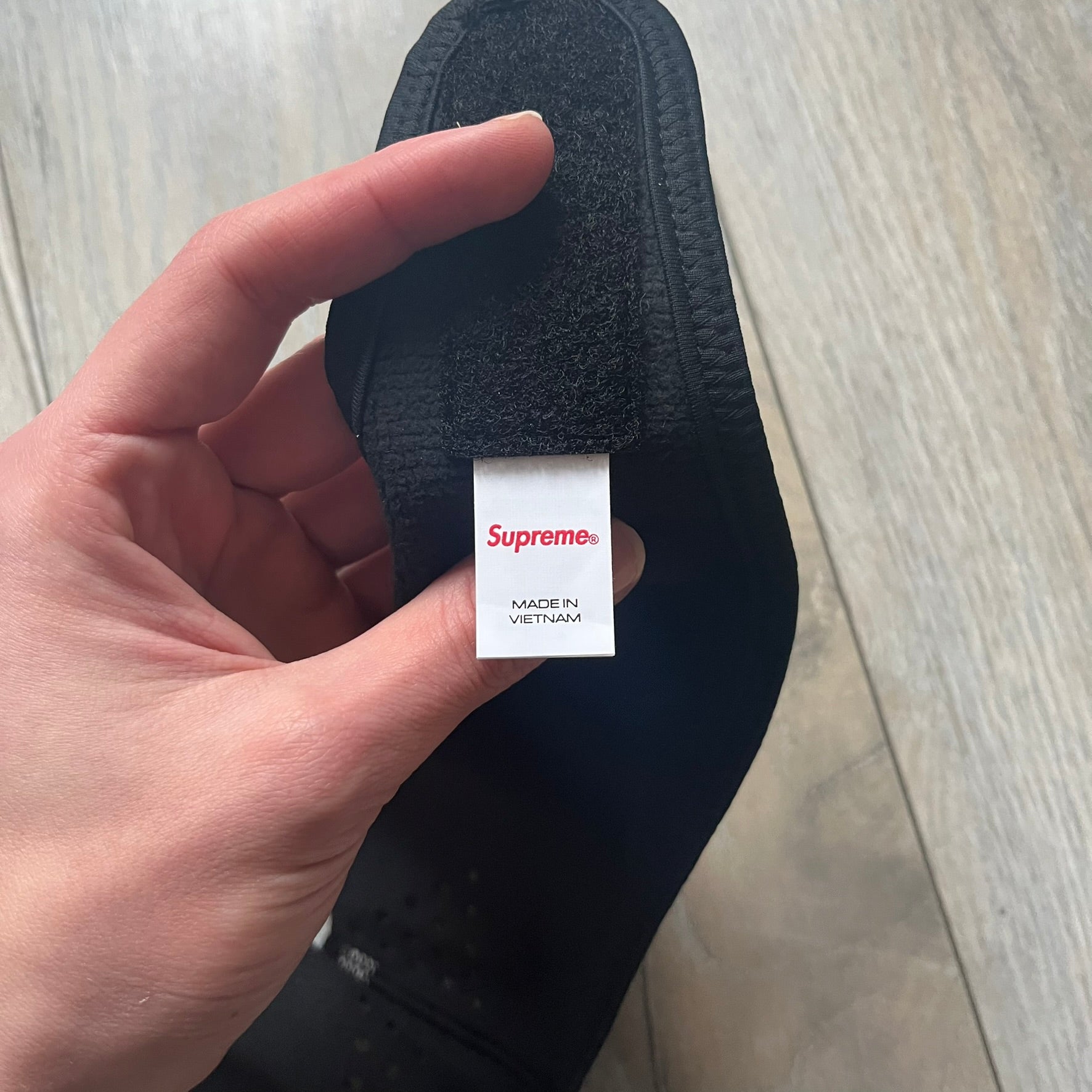 Supreme FW25 facemask produced in collaboration with GORE WINDSTOPPER® Labs, released on January 2, 2026. Constructed from water-resistant, windproof WINDSTOPPER® fabric with a fleece-bonded backing, designed for breathability and skin comfort. Features a Velcro flap closure, small front breathing perforations, nose and eye openings, a large white Supreme logo printed across the front, 3M reflective Supreme branding on the front and side, and a WINDSTOPPER® logo on the side. Finished in black.