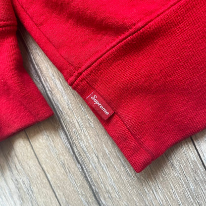 Supreme Catwoman FW23 Hooded Sweatshirt is a red pullover hoodie released on October 19, 2023. It features a drawstring hood, kangaroo pocket, and ribbed cuffs and hem. A small Supreme box logo is placed on the left chest in black.&nbsp;The back features a large Catwoman mask graphic combined with Supreme branding across the width of the design in black and green.