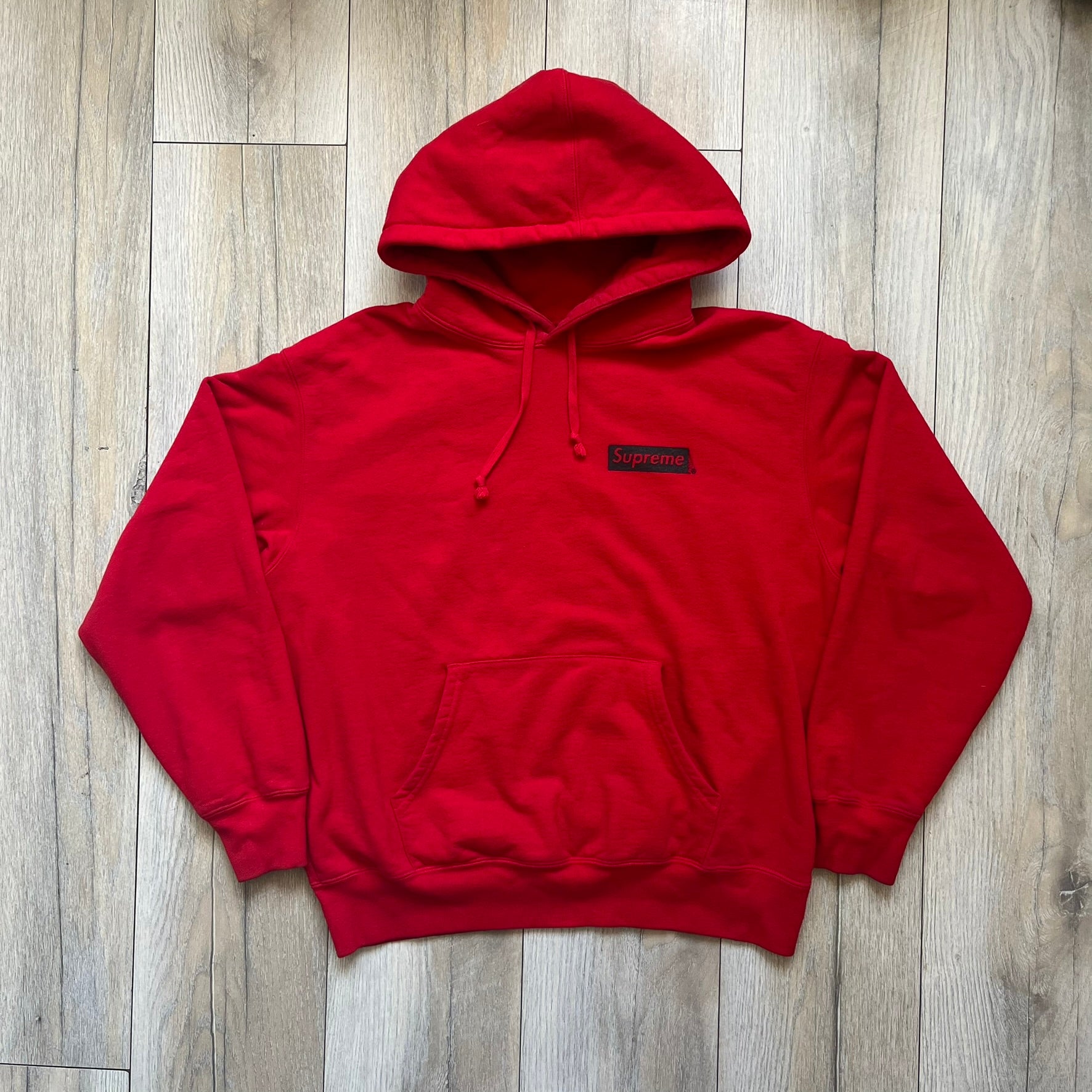 Supreme Catwoman FW23 Hooded Sweatshirt is a red pullover hoodie released on October 19, 2023. It features a drawstring hood, kangaroo pocket, and ribbed cuffs and hem. A small Supreme box logo is placed on the left chest in black.&nbsp;The back features a large Catwoman mask graphic combined with Supreme branding across the width of the design in black and green.
