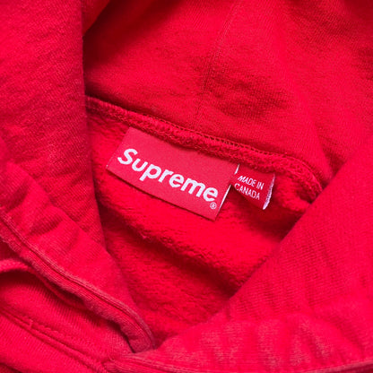 Supreme Catwoman FW23 Hooded Sweatshirt is a red pullover hoodie released on October 19, 2023. It features a drawstring hood, kangaroo pocket, and ribbed cuffs and hem. A small Supreme box logo is placed on the left chest in black.&nbsp;The back features a large Catwoman mask graphic combined with Supreme branding across the width of the design in black and green.