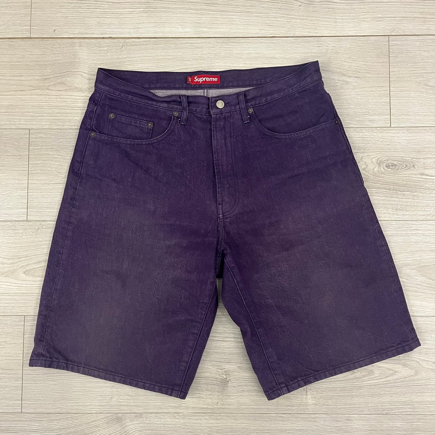 Supreme Denim Purple SS25 Baggy Shorts crafted from 13 oz. all-cotton denim in a purple hue. Features a relaxed baggy fit, classic five-pocket styling, zip fly, copper oxide rivets, and embroidered Supreme New York logo on the back pocket. Durable, stylish, and perfect for everyday streetwear.