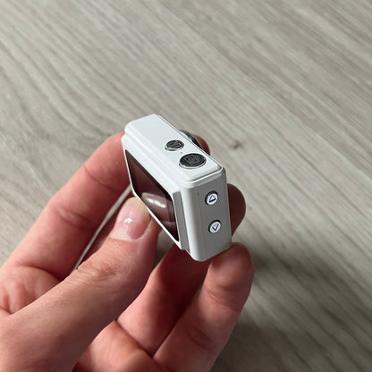 Supreme Digital Camera Keychain released for FW25 in white with a printed Supreme box logo on the front. This ultra-compact digital camera measures 1.92" x 1.14" x 1.1" and includes a 32GB TF card, USB-C cable, and built-in 1080p HD recording. When powered on, the screen displays the Supreme logo, with selectable interface colors in colors like: pink, green, or blue.