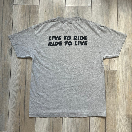 Supreme FW07 WTAPS “Live To Ride, Ride To Live” Gray Tee is a gray short-sleeve T-shirt released in Autumn/Winter 2007. The front features a black sketch of Robin on a skateboard with a small red Supreme logo beside it, while the upper back displays bold “Live To Ride, Ride To Live” text. The T-shirt was designed by Tetsu Nishiyama (WTAPS).