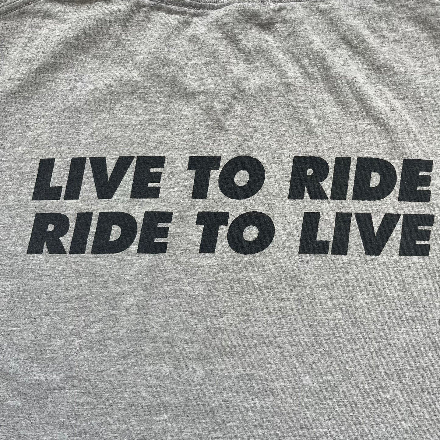 Supreme FW07 WTAPS “Live To Ride, Ride To Live” Gray Tee is a gray short-sleeve T-shirt released in Autumn/Winter 2007. The front features a black sketch of Robin on a skateboard with a small red Supreme logo beside it, while the upper back displays bold “Live To Ride, Ride To Live” text. The T-shirt was designed by Tetsu Nishiyama (WTAPS).