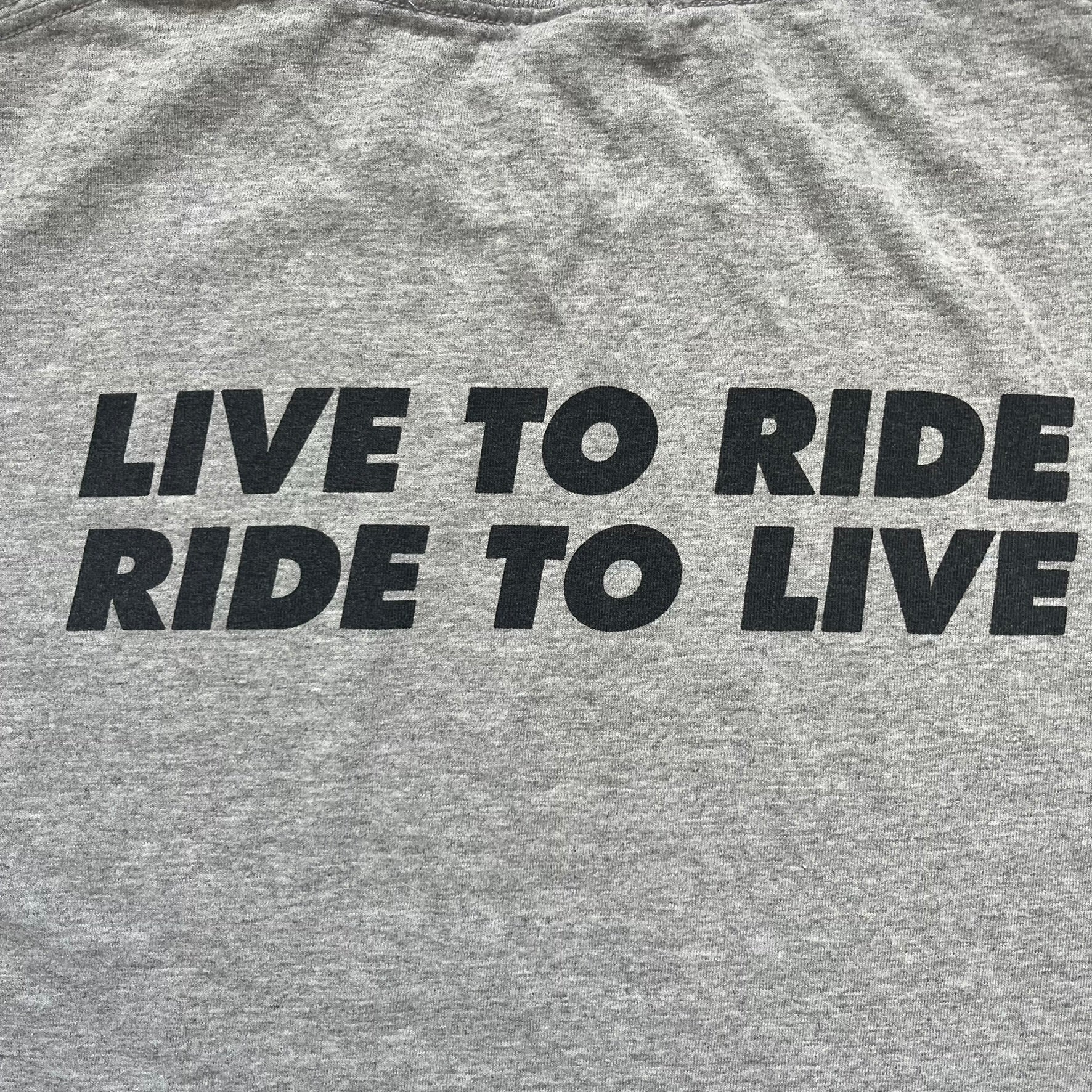 Supreme FW07 WTAPS “Live To Ride, Ride To Live” Gray Tee is a gray short-sleeve T-shirt released in Autumn/Winter 2007. The front features a black sketch of Robin on a skateboard with a small red Supreme logo beside it, while the upper back displays bold “Live To Ride, Ride To Live” text. The T-shirt was designed by Tetsu Nishiyama (WTAPS).