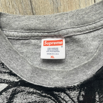 Supreme FW07 WTAPS “Live To Ride, Ride To Live” Gray Tee is a gray short-sleeve T-shirt released in Autumn/Winter 2007. The front features a black sketch of Robin on a skateboard with a small red Supreme logo beside it, while the upper back displays bold “Live To Ride, Ride To Live” text. The T-shirt was designed by Tetsu Nishiyama (WTAPS).