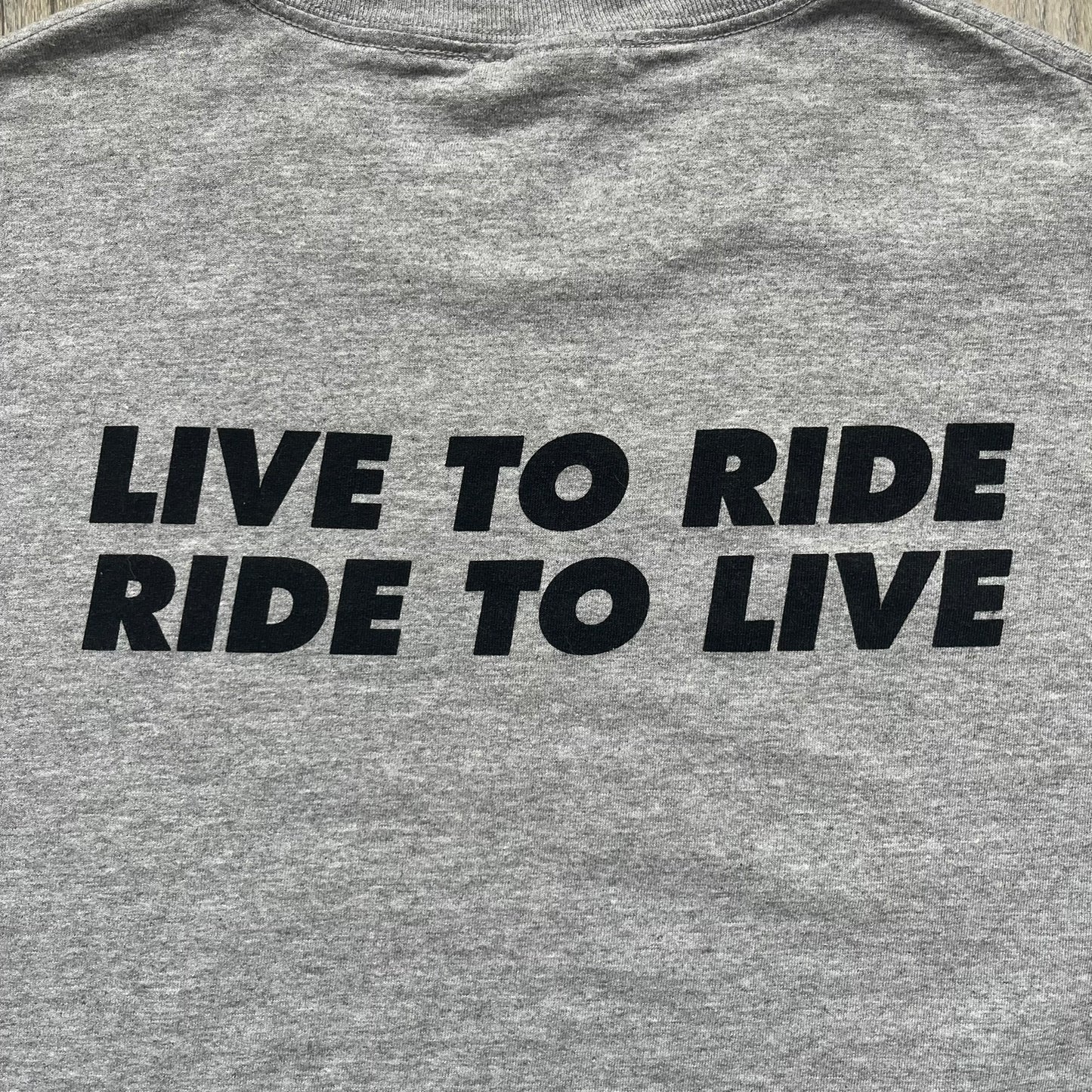 Supreme FW07 WTAPS “Live To Ride, Ride To Live” Gray Tee is a gray short-sleeve T-shirt released in Autumn/Winter 2007. The front features a black sketch of Robin on a skateboard with a small red Supreme logo beside it, while the upper back displays bold “Live To Ride, Ride To Live” text. The T-shirt was designed by Tetsu Nishiyama (WTAPS).