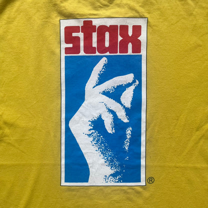 Supreme FW12 Stax Records Tee is a yellow T-shirt from the Fall/Winter 2012 collection. The front features small black Supreme text on the left chest. The back has a large Stax Records logo print with the blue and white hand graphic and red Stax text underneath. Concord Music Group licensing on the necktag.