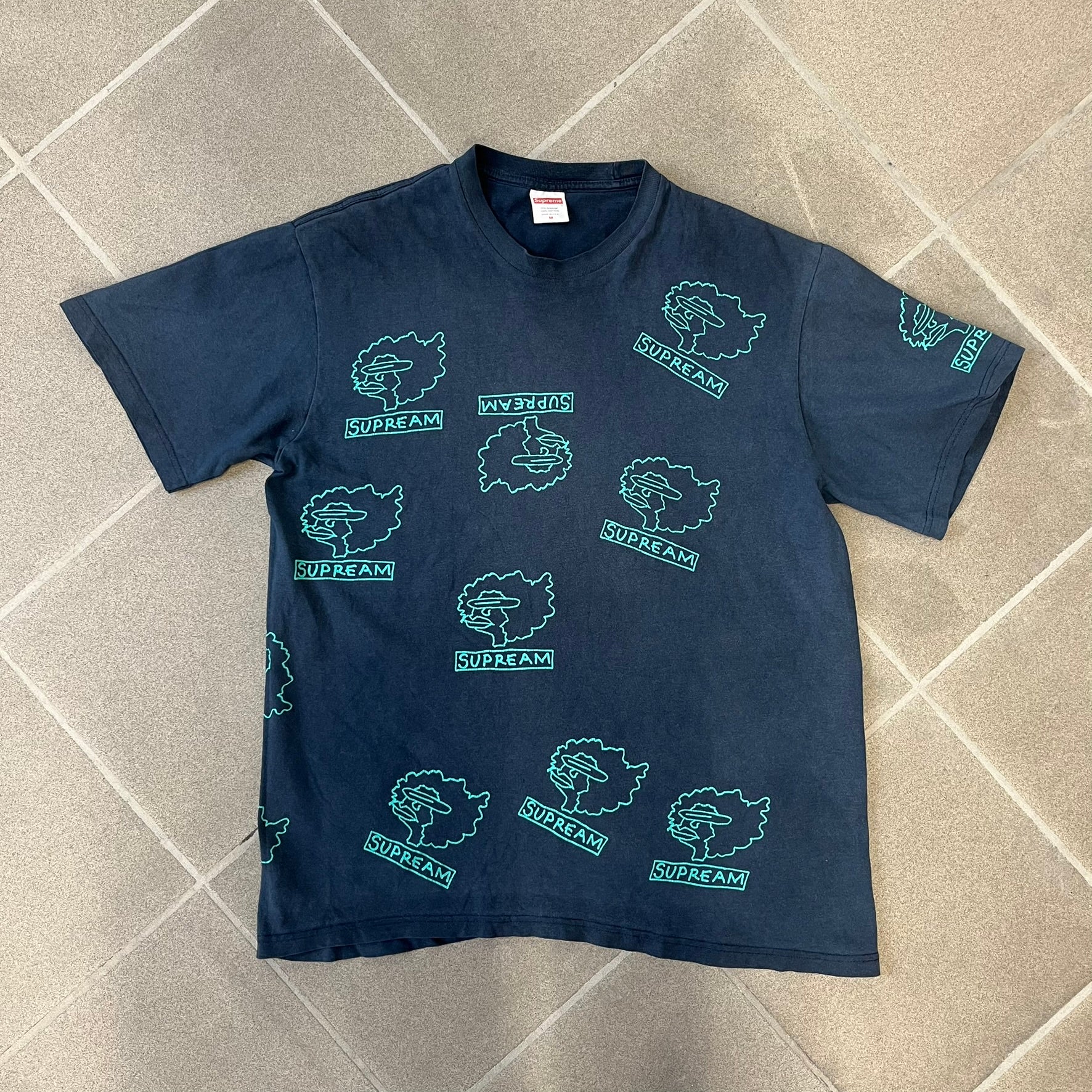 Supreme FW17 Gonz Heads Tee is a navy T-shirt from the Fall/Winter 2017 collection created in collaboration with Mark Gonzales (The Gonz). The tee features repeated green Gonz head graphics printed across both the front and back in different orientations. The shirt is made in the USA.

