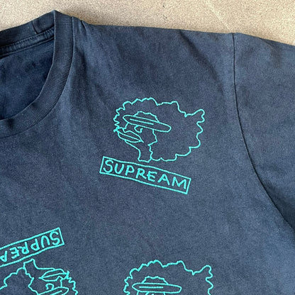 Supreme FW17 Gonz Heads Tee is a navy T-shirt from the Fall/Winter 2017 collection created in collaboration with Mark Gonzales (The Gonz). The tee features repeated green Gonz head graphics printed across both the front and back in different orientations. The shirt is made in the USA.
