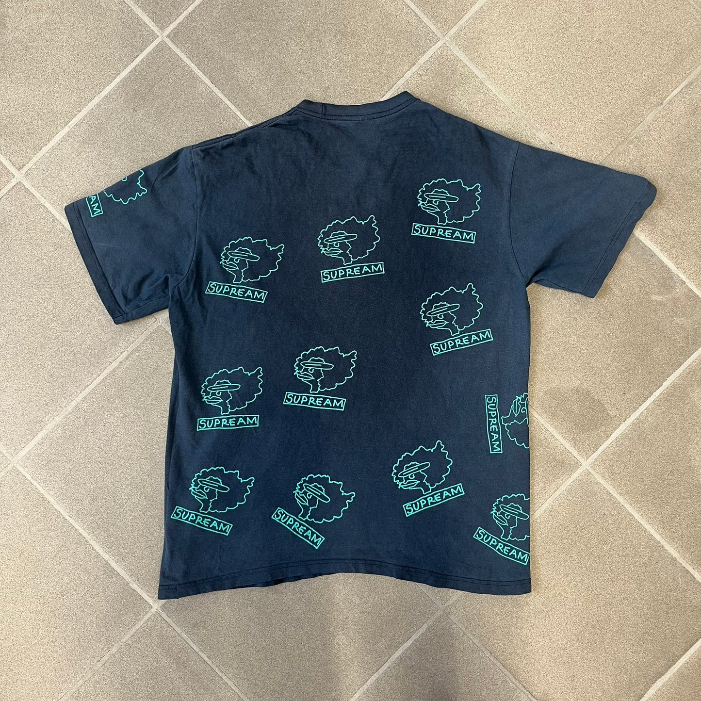 Supreme FW17 Gonz Heads Tee is a navy T-shirt from the Fall/Winter 2017 collection created in collaboration with Mark Gonzales (The Gonz). The tee features repeated green Gonz head graphics printed across both the front and back in different orientations. The shirt is made in the USA.
