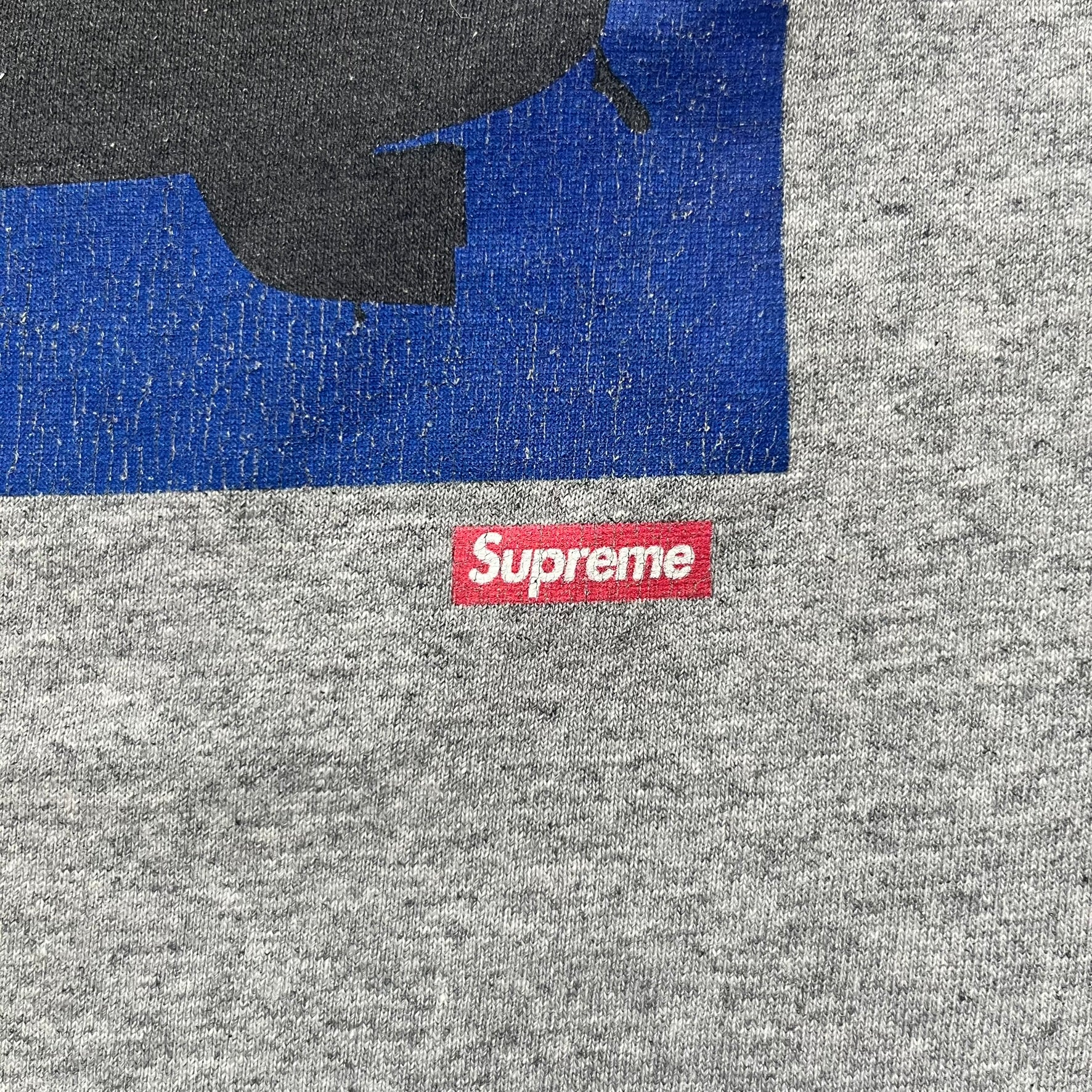 Supreme FW17 Scarface Blimp Gray Tee is a grey T-shirt from the Fall/Winter 2017 collection featuring a large front print from the film Scarface. The graphic shows the blimp scene with “The World Is Yours” text in black on a blue background, with a small red Supreme box logo printed below. Released in October 2017 as part of the Supreme x Scarface collaboration.