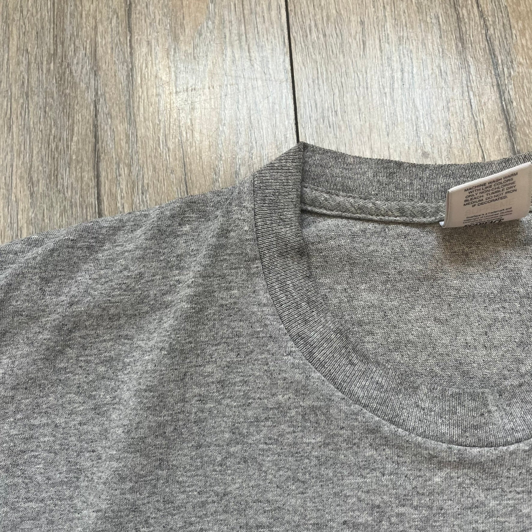 Supreme FW17 Scarface Blimp Gray Tee is a grey T-shirt from the Fall/Winter 2017 collection featuring a large front print from the film Scarface. The graphic shows the blimp scene with “The World Is Yours” text in black on a blue background, with a small red Supreme box logo printed below. Released in October 2017 as part of the Supreme x Scarface collaboration.