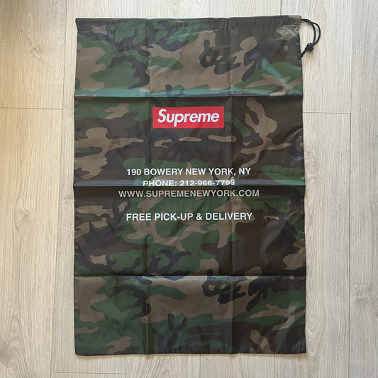 Supreme FW25 Woodland Camo laundry bag in Realtree AP camouflage, released as a limited gift during the first drop of the Fall/Winter 2025 season. Features 190 Bowery New York contact details, “Free Pick-up &amp; Delivery” text, and the iconic Supreme Box Logo on the top.