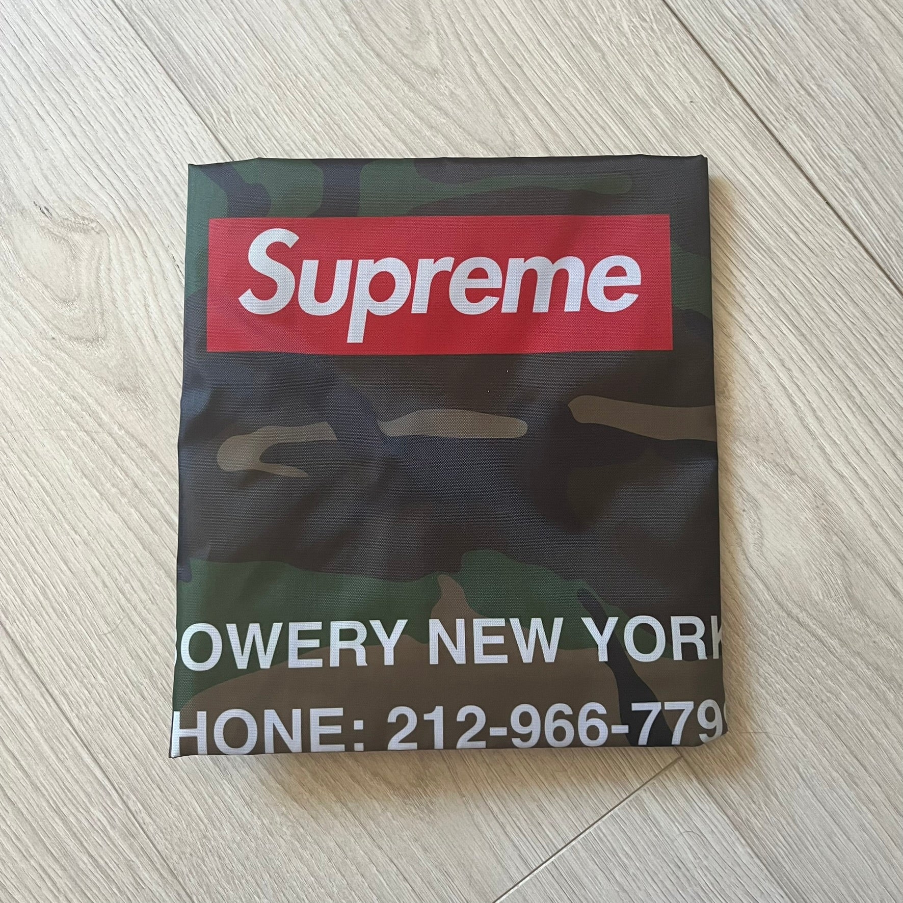 Supreme FW25 Woodland Camo laundry bag in Realtree AP camouflage, released as a limited gift during the first drop of the Fall/Winter 2025 season. Features 190 Bowery New York contact details, “Free Pick-up &amp; Delivery” text, and the iconic Supreme Box Logo on the top.