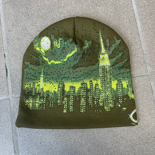 Supreme FW26 Cityscape Art Dealer Green&nbsp; Beanie is a green acrylic beanie with original artwork by Art Dealer, featuring a lime and dark green night city graphic with a moon and small stars across the sky on both sides. An old English-style Supreme logo sits on the front, and rhinestone appliqués in different sizes decorate the front and back. The print is stretchy, so any cracking effect that appears is just the print stretching with wear.