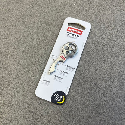 Supreme FW26 Nite Ize Skull Key Tool features a silver-tone multi-purpose key tool with a skull-shaped top and a red Supreme logo underneath. The tool includes a file, bottle opener, serrated edge, scoring point, and screwdriver.
