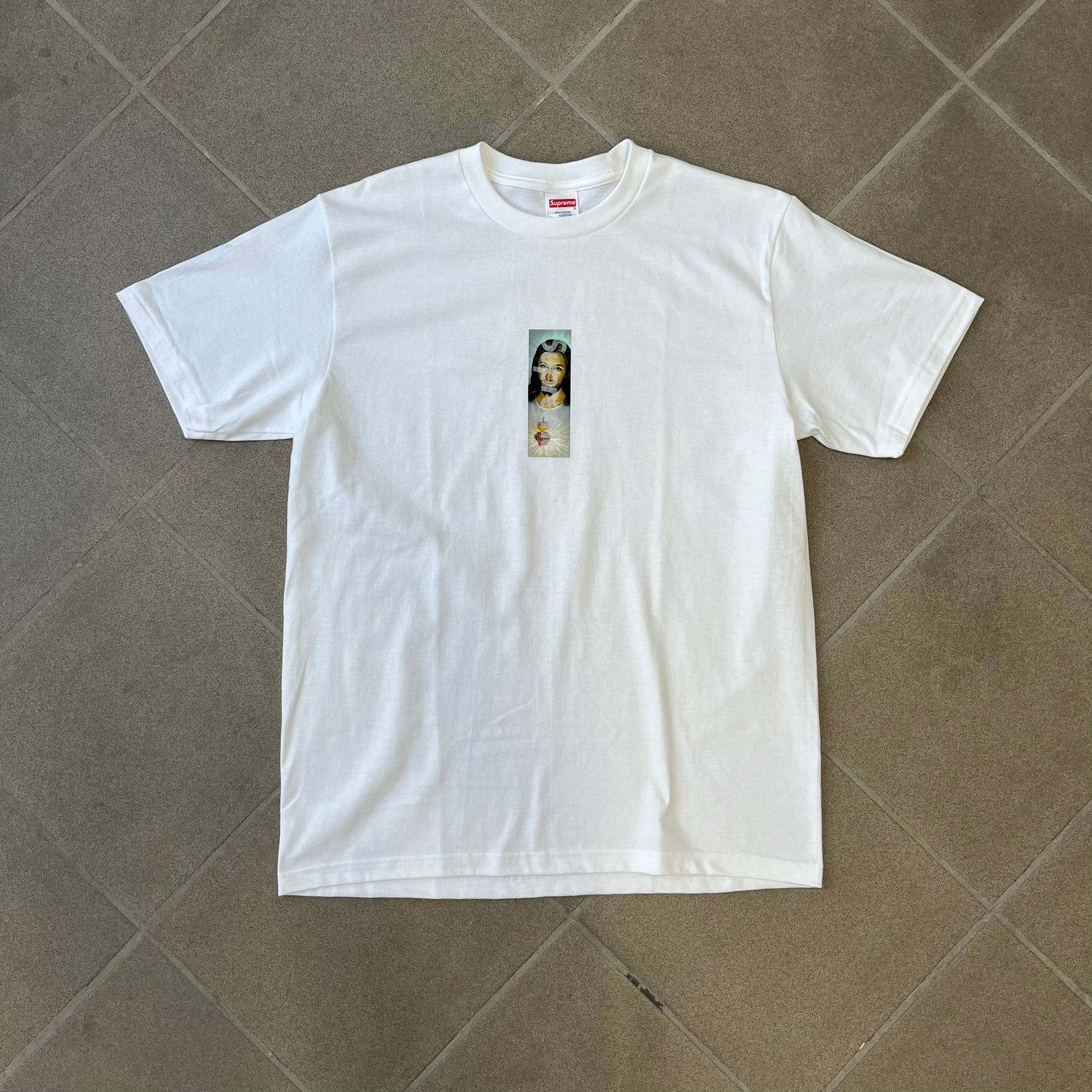 Supreme FW26 Prayer Card Jesus Box Logo White Tee features a white 100% cotton T-shirt with a vertical Supreme box logo graphic on the front. The Supreme text is printed lightly over a graphic depicting the Sacred Heart of Jesus. Made in Honduras.
