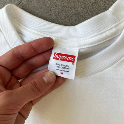 Supreme FW26 Prayer Card Jesus Box Logo White Tee features a white 100% cotton T-shirt with a vertical Supreme box logo graphic on the front. The Supreme text is printed lightly over a graphic depicting the Sacred Heart of Jesus. Made in Honduras.
