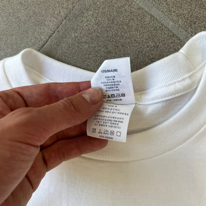 Supreme FW26 Prayer Card Jesus Box Logo White Tee features a white 100% cotton T-shirt with a vertical Supreme box logo graphic on the front. The Supreme text is printed lightly over a graphic depicting the Sacred Heart of Jesus. Made in Honduras.
