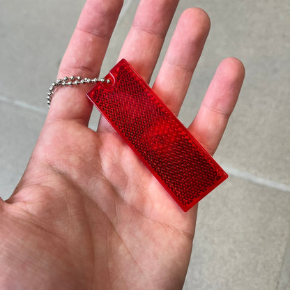Supreme FW26 Reflective Red Keychain is a red plastic keychain on a steel ball chain, with a Supreme logo on the front. The back is made of small reflective panels.