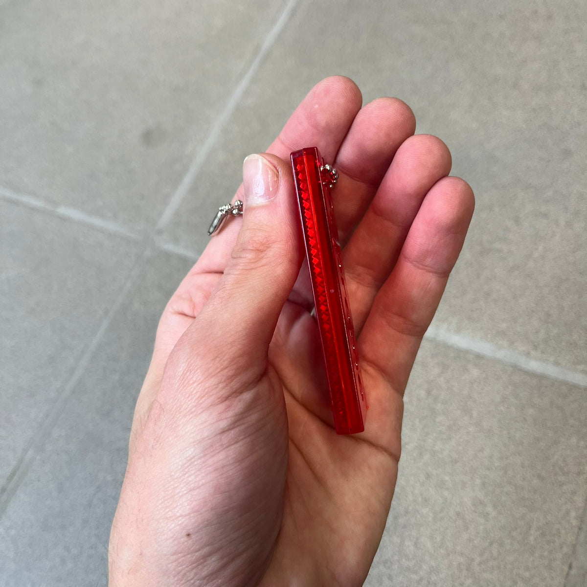 Supreme FW26 Reflective Red Keychain is a red plastic keychain on a steel ball chain, with a Supreme logo on the front. The back is made of small reflective panels.