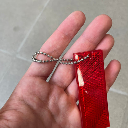 Supreme FW26 Reflective Red Keychain is a red plastic keychain on a steel ball chain, with a Supreme logo on the front. The back is made of small reflective panels.