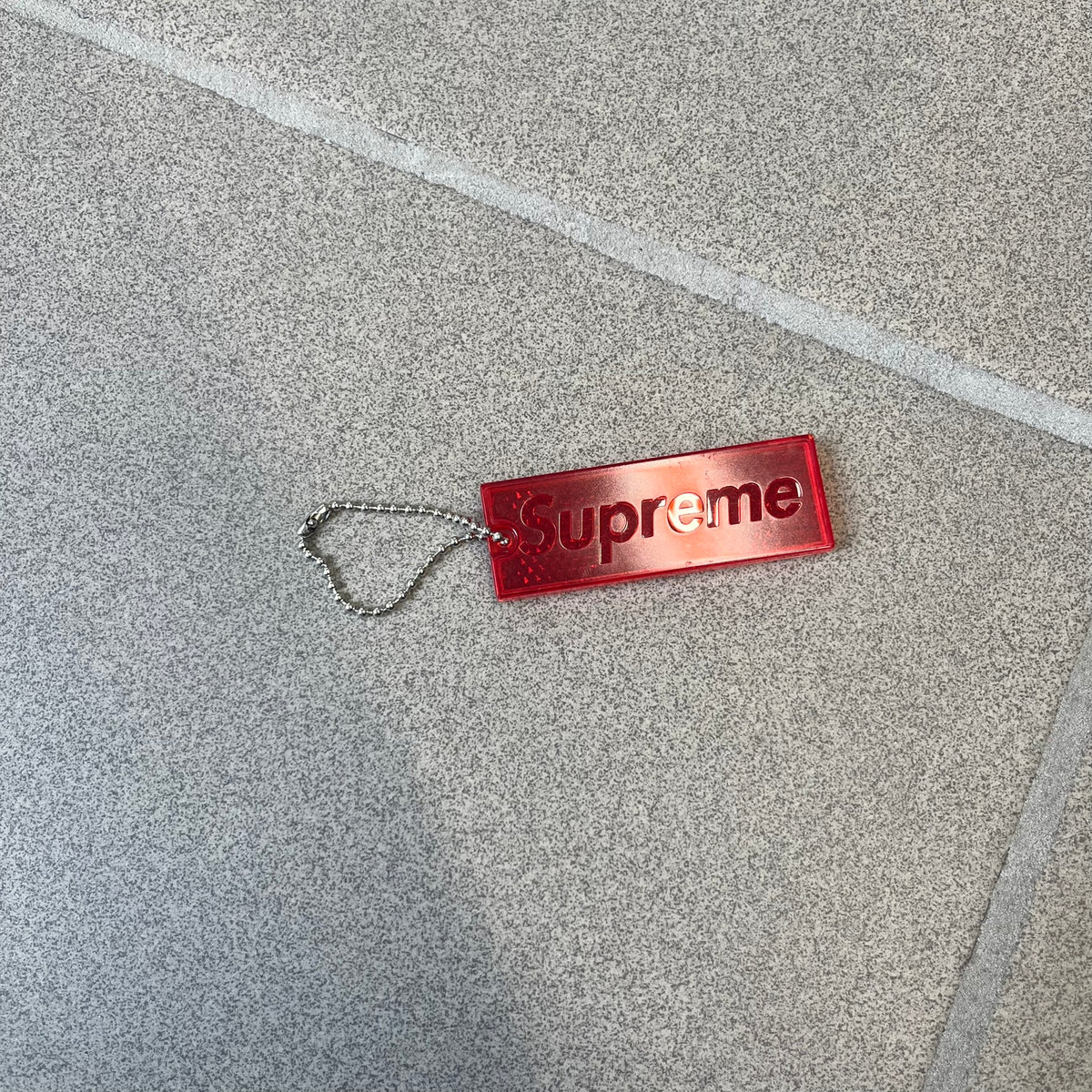 Supreme FW26 Reflective Red Keychain is a red plastic keychain on a steel ball chain, with a Supreme logo on the front. The back is made of small reflective panels.