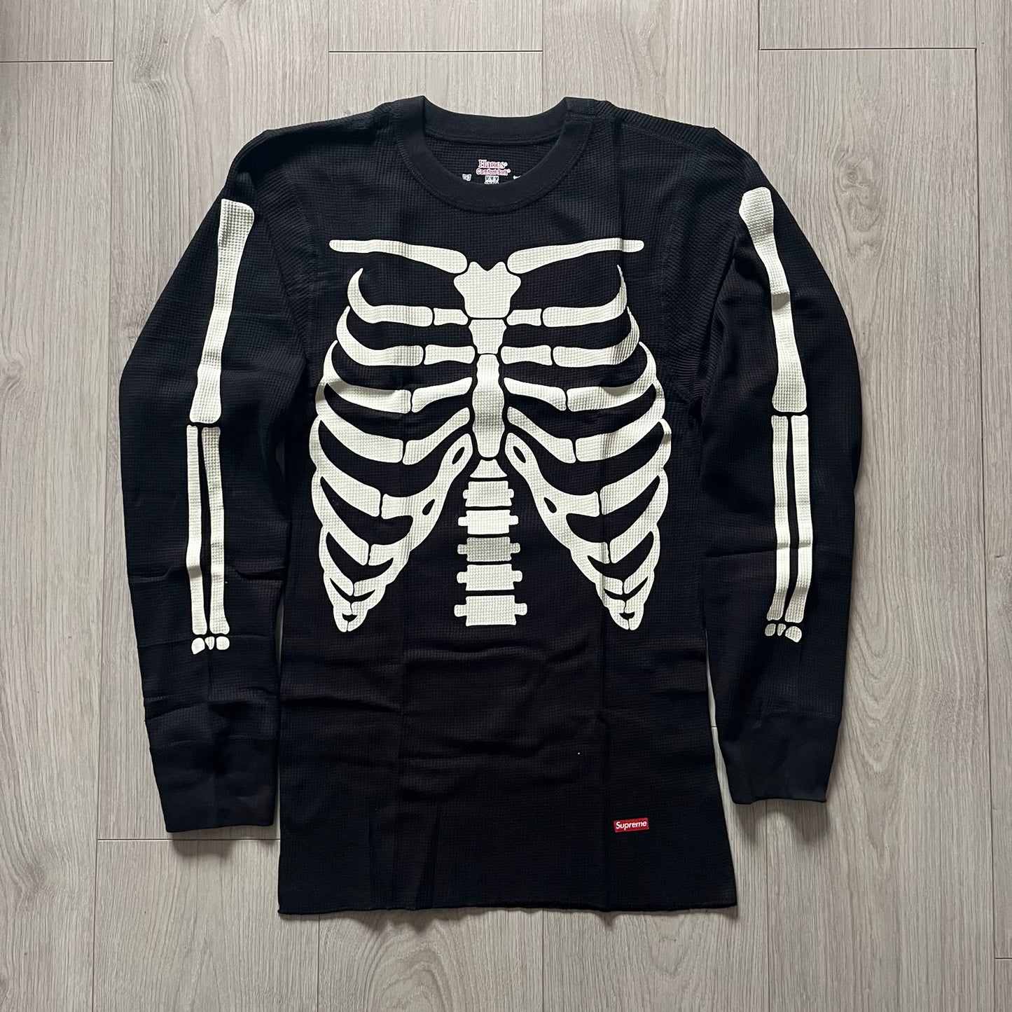 Supreme Hanes Bones Thermal Crew from FW25, crafted from 100% cotton in black with white bone graphics. Features a ribcage-inspired skeleton print on the front, matching arm bone designs on the sleeves, and a small Supreme logo near the hem. Released on October 23, 2025.