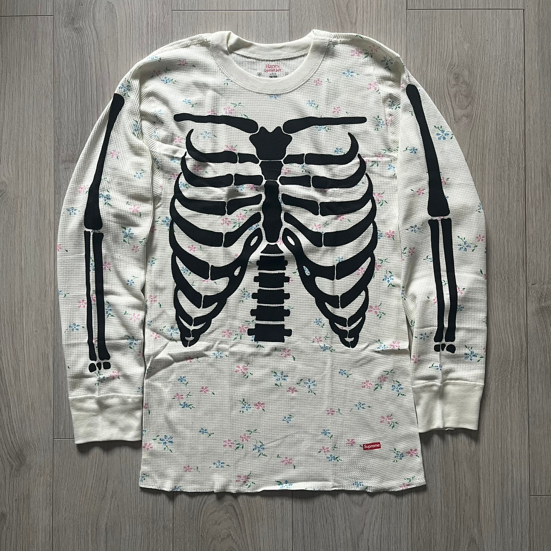 Supreme Hanes Bones Thermal Crew from FW25, crafted from 100% cotton in natural/white with black bone graphics and small floral all over print. Features a ribcage-inspired skeleton print on the front, matching arm bone designs on the sleeves, and a small Supreme logo near the hem. Released on October 23, 2025.