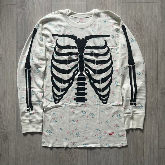 Supreme Hanes Bones Thermal Crew from FW25, crafted from 100% cotton in natural/white with black bone graphics and small floral all over print. Features a ribcage-inspired skeleton print on the front, matching arm bone designs on the sleeves, and a small Supreme logo near the hem. Released on October 23, 2025.