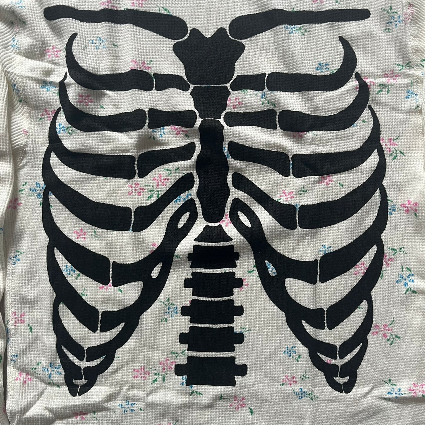 Supreme Hanes Bones Thermal Crew from FW25, crafted from 100% cotton in natural/white with black bone graphics and small floral all over print. Features a ribcage-inspired skeleton print on the front, matching arm bone designs on the sleeves, and a small Supreme logo near the hem. Released on October 23, 2025.