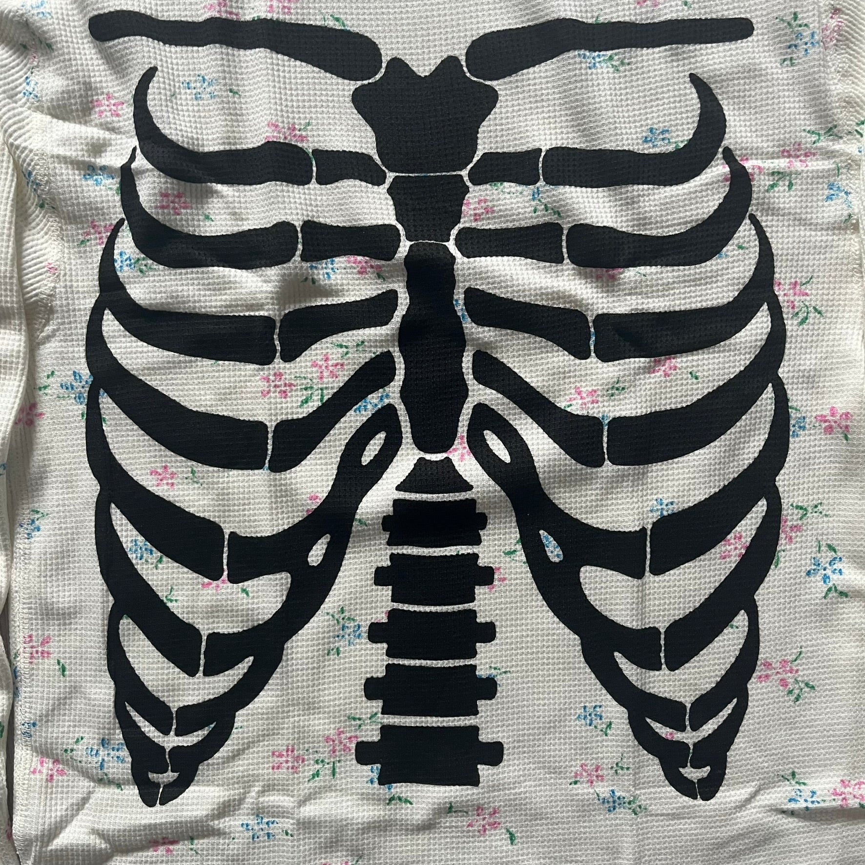 Supreme Hanes Bones Thermal Crew from FW25, crafted from 100% cotton in natural/white with black bone graphics and small floral all over print. Features a ribcage-inspired skeleton print on the front, matching arm bone designs on the sleeves, and a small Supreme logo near the hem. Released on October 23, 2025.
