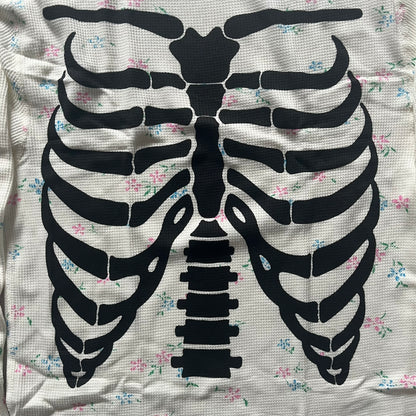 Supreme Hanes Bones Thermal Crew from FW25, crafted from 100% cotton in natural/white with black bone graphics and small floral all over print. Features a ribcage-inspired skeleton print on the front, matching arm bone designs on the sleeves, and a small Supreme logo near the hem. Released on October 23, 2025.