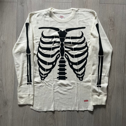 Supreme Hanes Bones Thermal Crew from FW25, crafted from 100% cotton in natural/white with black bone graphics. Features a ribcage-inspired skeleton print on the front, matching arm bone designs on the sleeves, and a small Supreme logo near the hem. Released on October 23, 2025.