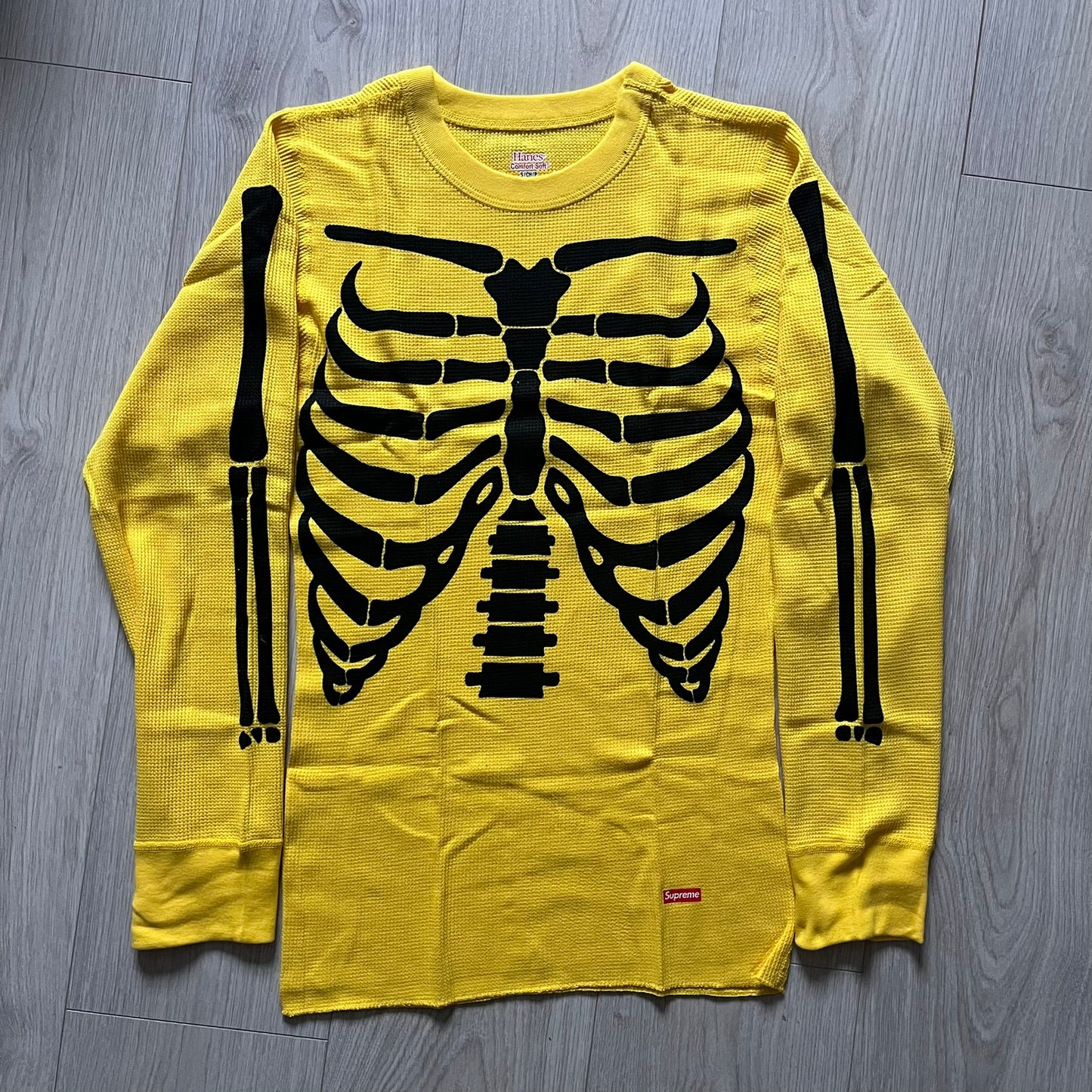 Supreme Hanes Bones Thermal Crew from FW25, crafted from 100% cotton in yellow with black bone graphics. Features a ribcage-inspired skeleton print on the front, matching arm bone designs on the sleeves, and a small Supreme logo near the hem. Released on October 23, 2025.