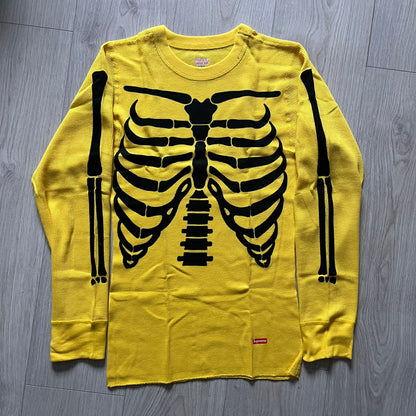 Supreme Hanes Bones Thermal Crew from FW25, crafted from 100% cotton in yellow with black bone graphics. Features a ribcage-inspired skeleton print on the front, matching arm bone designs on the sleeves, and a small Supreme logo near the hem. Released on October 23, 2025.