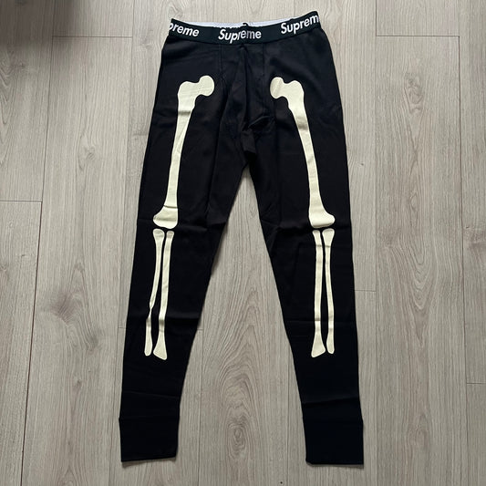  Supreme Hanes Bones Thermal Pant FW25 in black, crafted from 100% cotton. Features white skeletal bone prints running down both legs and a black elastic waistband with white Supreme branding throughout. Released October 23, 2025.